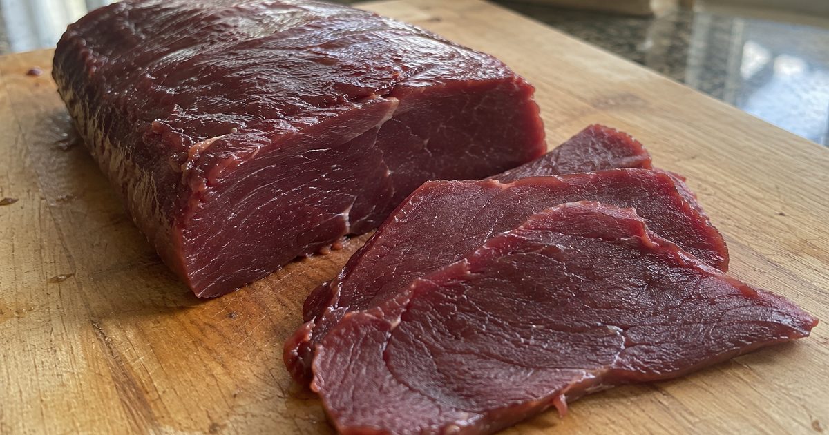 木のまな板の上の鹿肉(赤身)のブロックと、薄切りにした数枚のクローズアップ