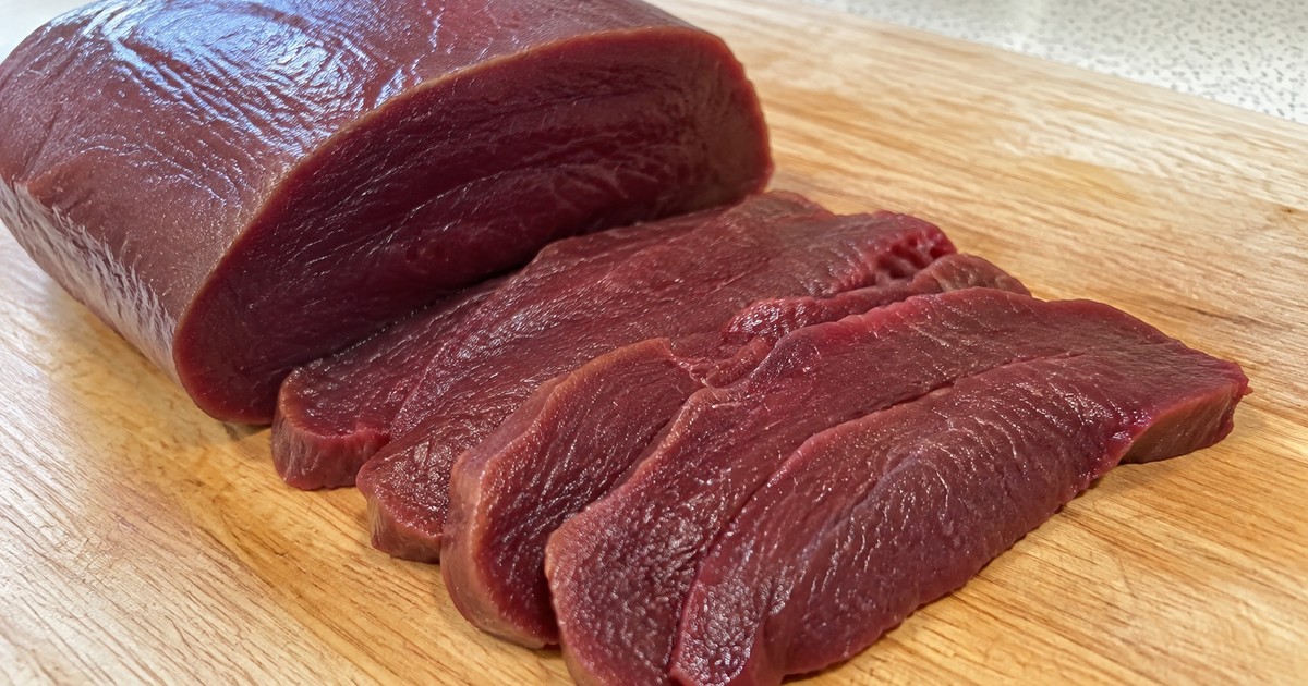 木のまな板の上の馬肉（赤身）のブロックと、薄切りにした数枚のクローズアップ